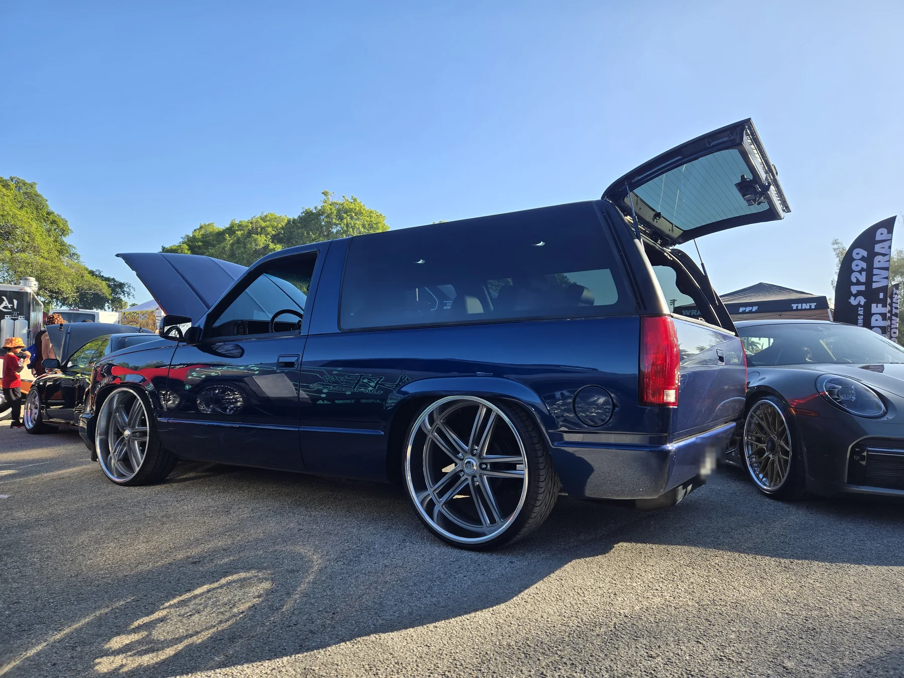 Dark blue custom SUV on oversized wheels at an outdoor Miami car show
