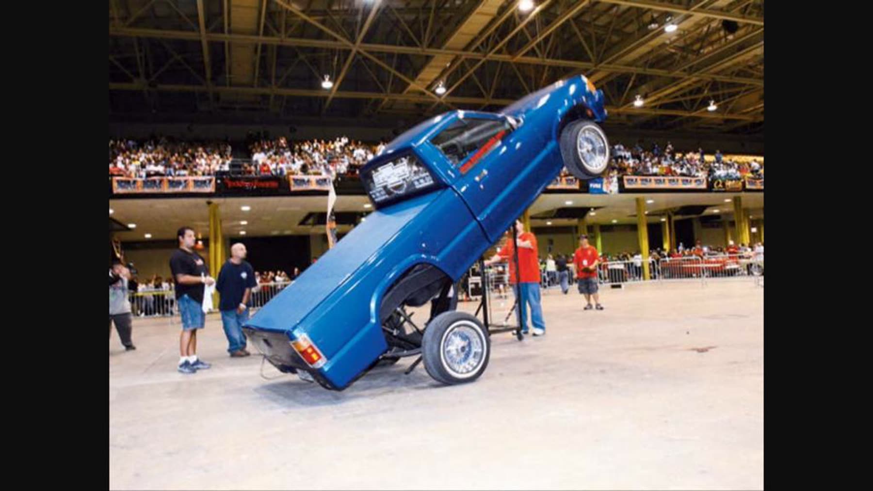 Blue custom truck lifting on hydraulics before a crowd at a car show